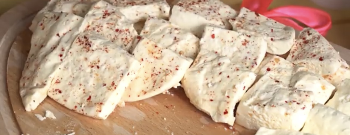 Close-up of cheese, cut into rectangular pieces and sprinkled with spices, displayed on a wooden serving board. 