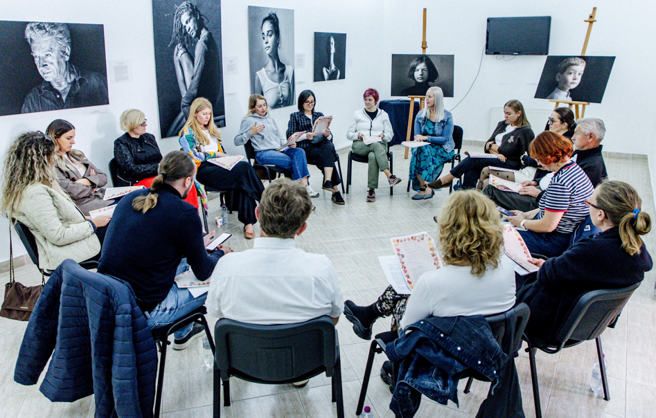 Participants sit in a large circle in a gallery and reflect together during a bibliotherapy-inspired activity.