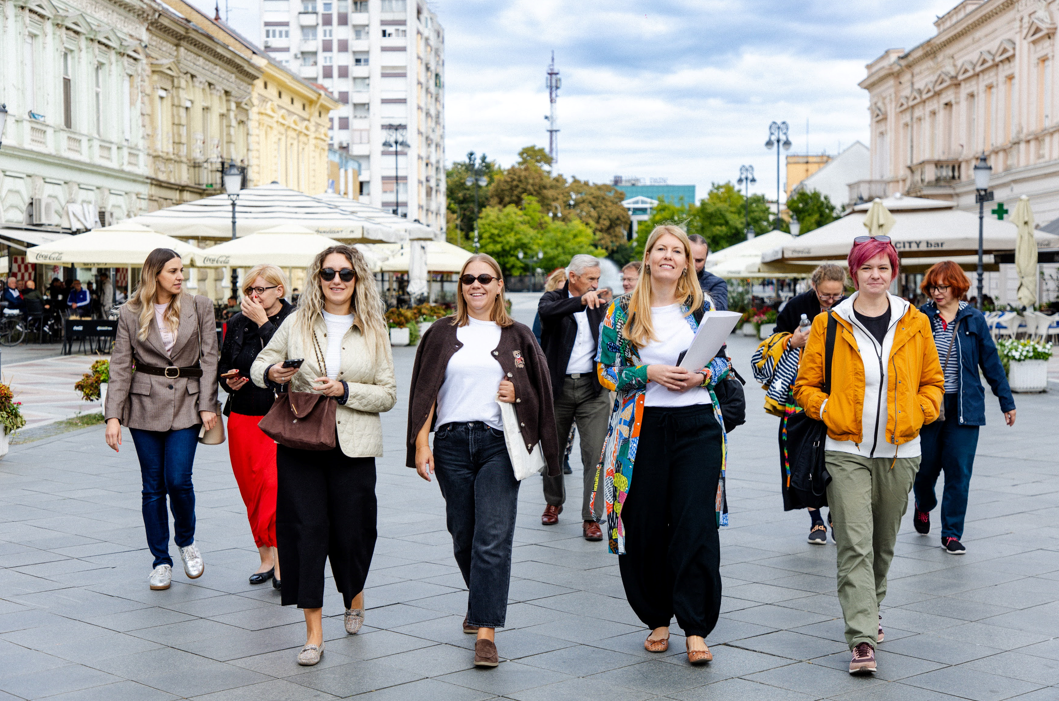 Pilot participants walk together through the central pedestrian area of Slavonski Brod while holding programme materials and talking.