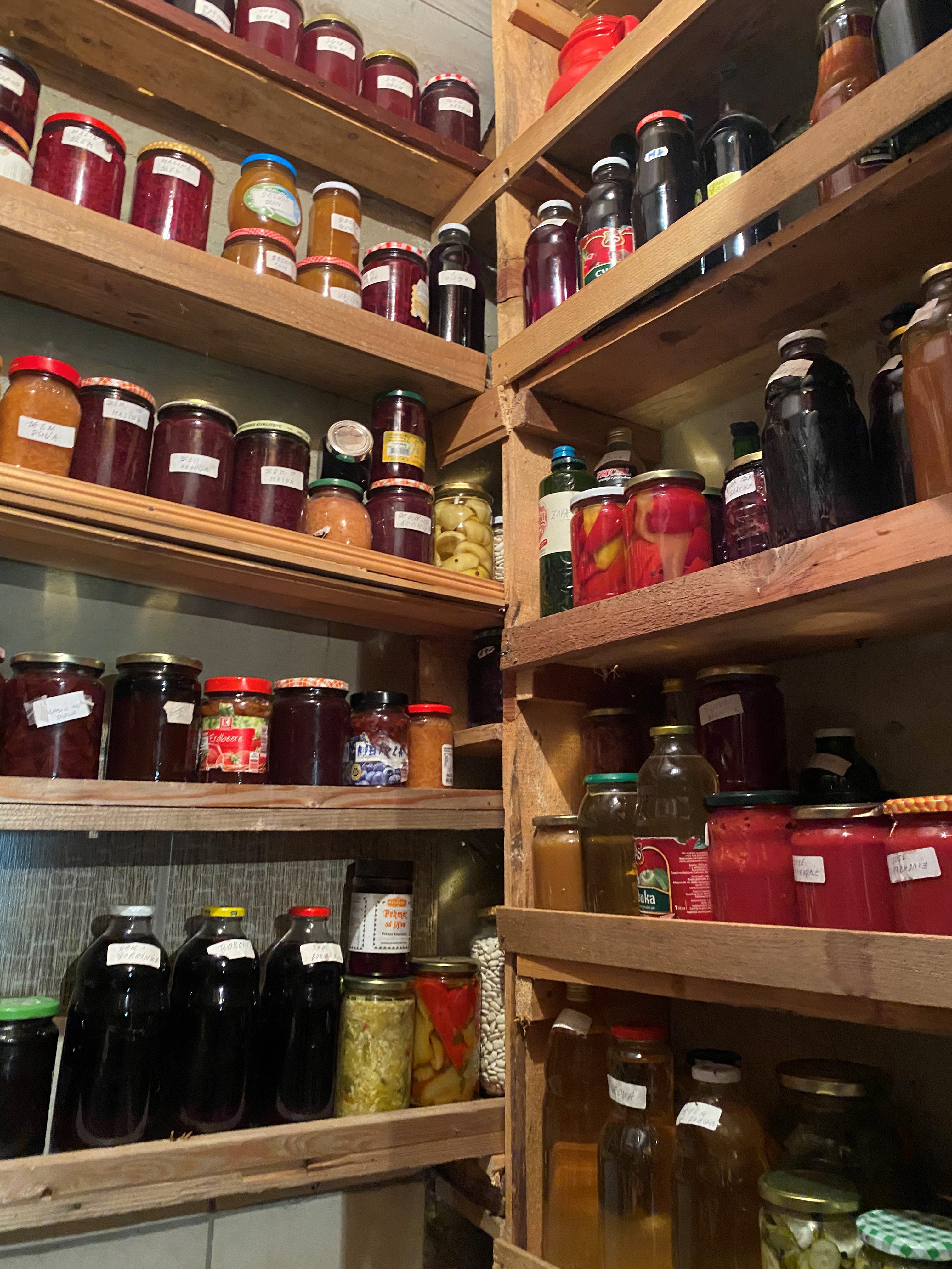 A well-organized pantry showcasing shelves filled with homemade preserves, including jars of jams, pickles, and juices.