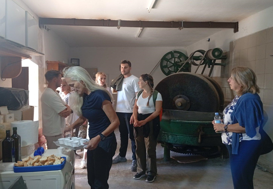 Visitors gather inside Pelinovo's old stone mill beside traditional olive-processing equipment and local products.